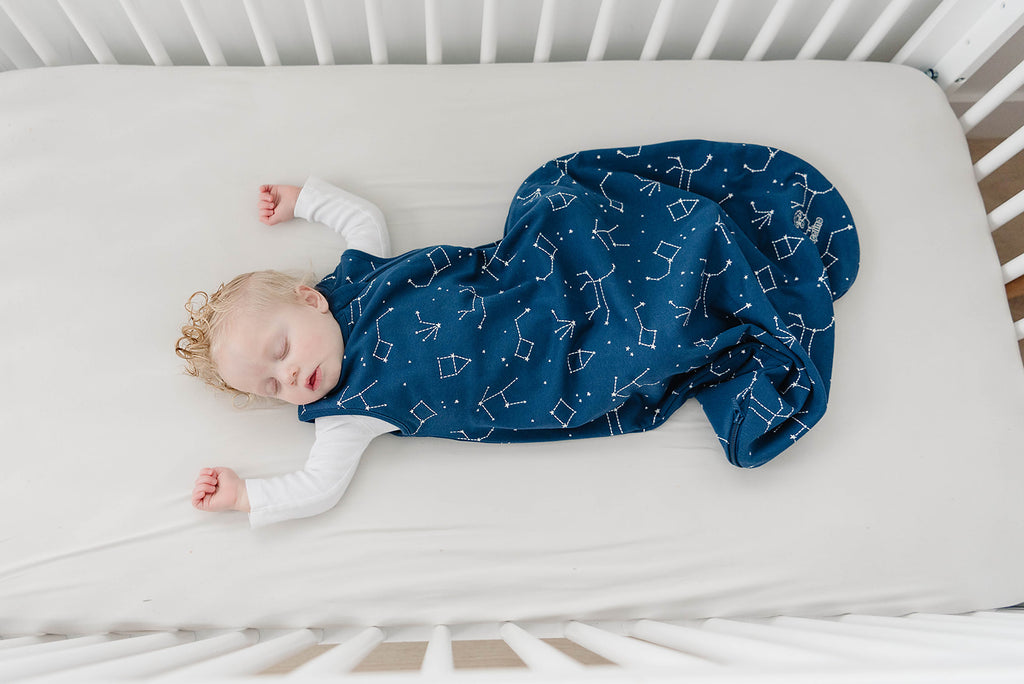 Sleeping baby in crib wearing a Woolino 4 Season® Basic Merino Wool Sleep Bag in Night Sky print