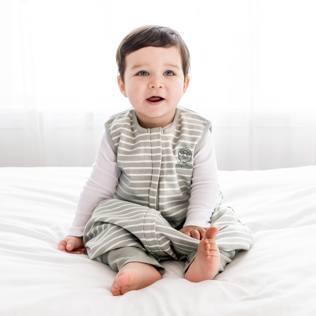 Toddler sitting on bed wearing a Woolino 4 Season® Sleep Bag With Feet