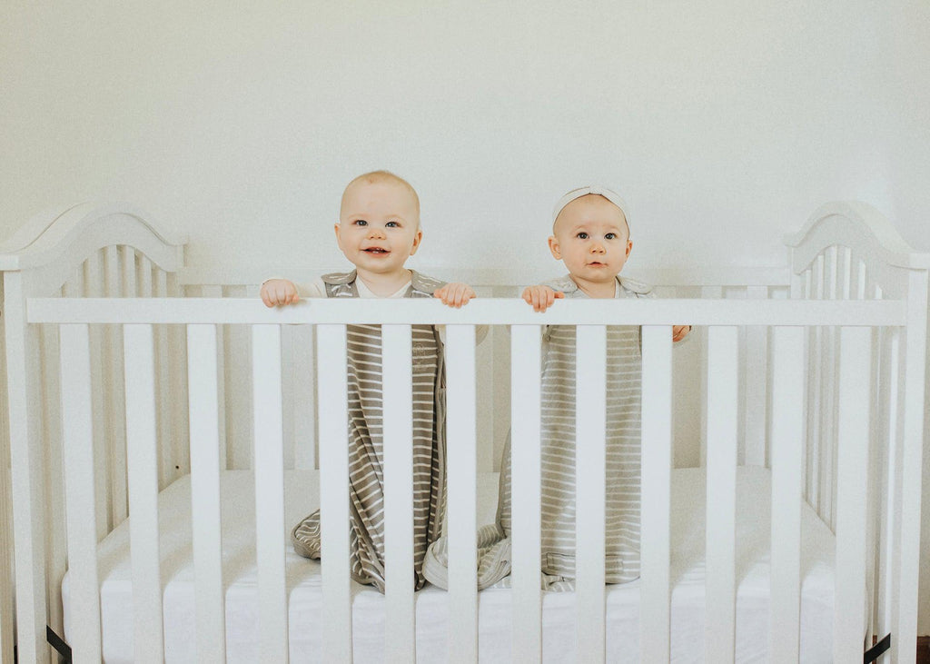 Twin babies wearing Woolino sleep sacks and standing in their shared crib.