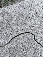 Image of snowflakes settled on a rusty steel surface with the laser cut word of "Evenlode" just visible through the snow.