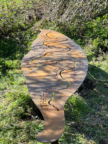 A portrait image of a large, rusty coloured, willlow leaf. Laser cut within the leaf shape is an aerial view of the River Evenlode's path, with text running alongside the curves of the river shape.