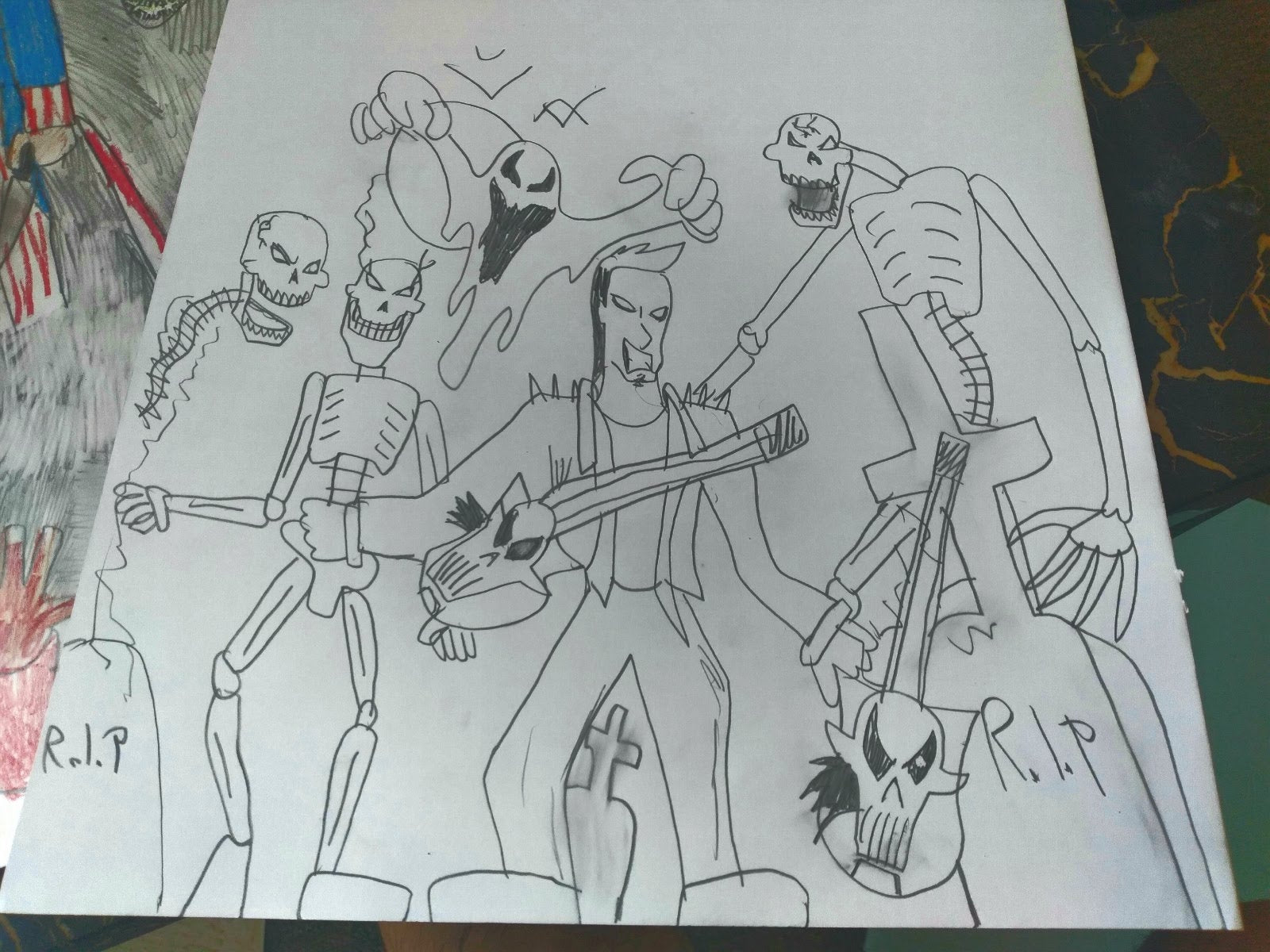 a pencil drawing on white paper, photographed against a stack of other drawings. The image shows a figure holding a skull-and-bones shaped guitar standing in the center of the picture, surrounded by skeletons and ghosts and bats. There are several gravestones with "RIP" written across their surfaces scattered around the ground. The characters all seem to be smiling and cackling with evil grins, and posed like members of a metal band.