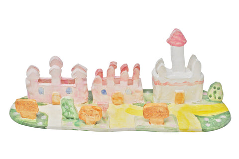 a glazed ceramic sculpture of a row of three miniature pink castles on neighboring green grass lawns