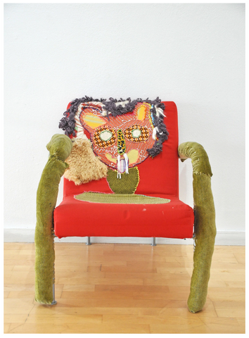 a red chair with green legs, embroidered with the face of a cat.
