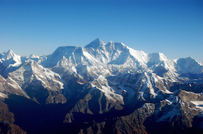 a photograph of the Himalayan mountains taken on a clear blue sky day as the sun is lighting their snow covered peaks.