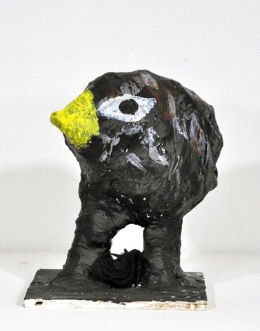 A paper mache sculpture of a small bird with a yellow beak and almond shaped eyes.