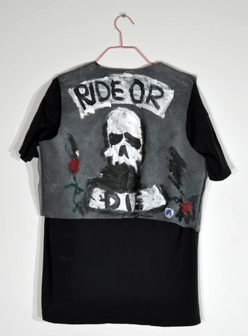 a black tshirt and jean jacket hanging on a hanger. the words "ride or die" are handpainted at the top and bottom of the jacket, with a skull painted in the middle.