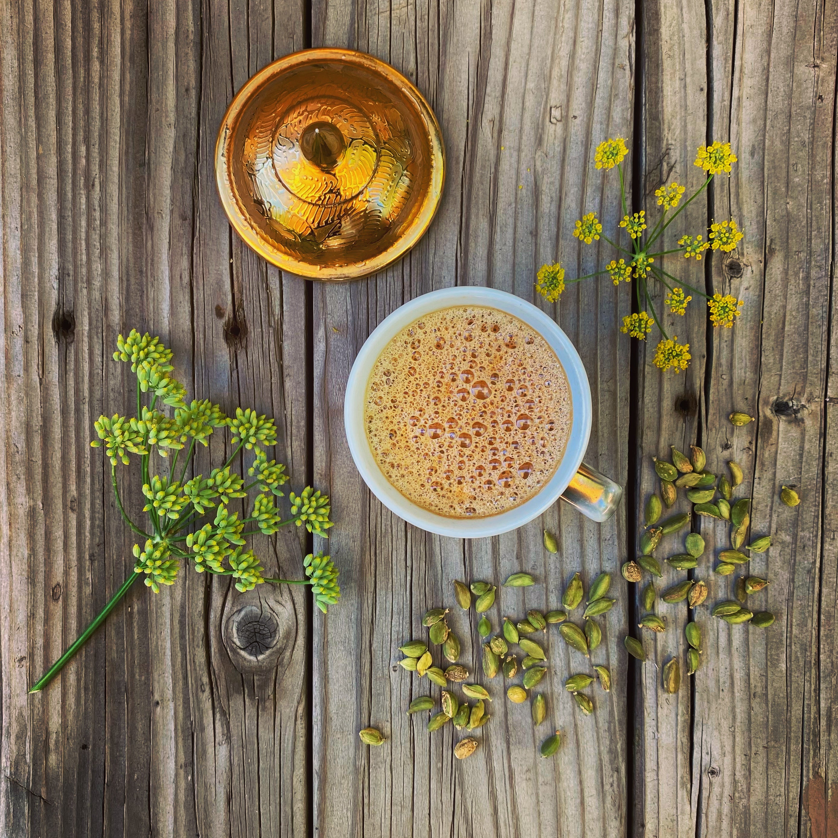 Cup of Honey Masala Chai with whole green cardamom pods and fennel blossoms on a wooden background
