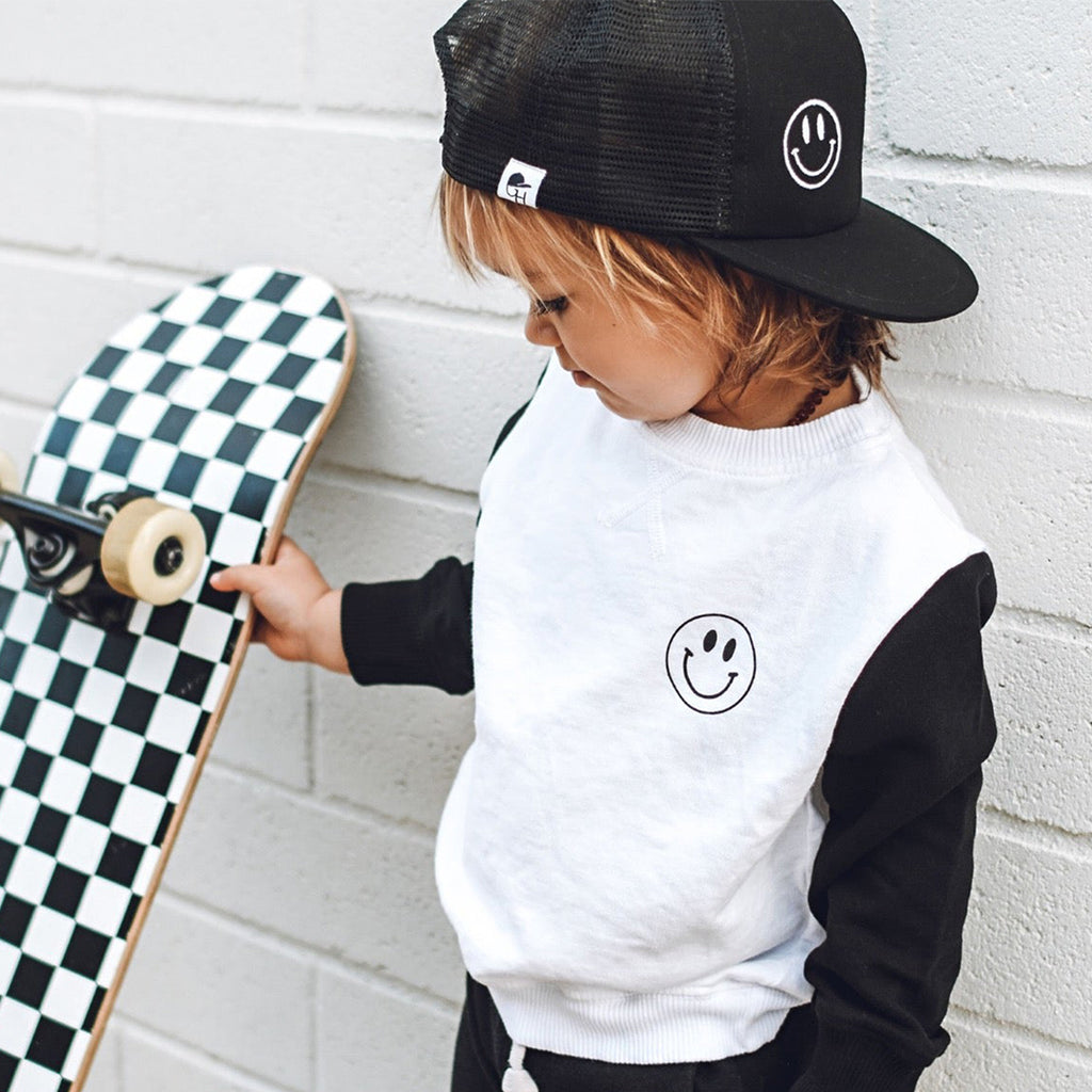 Child with a skateboard wearing matching Smiley Trucker Hat and Long sleeve t-shirt