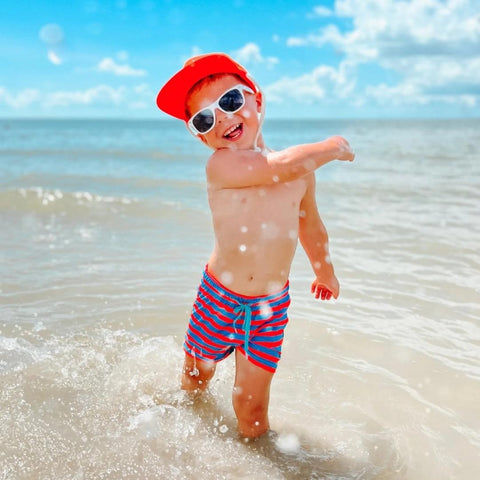Child playing in the water wearing brightly colored swim trunks and hat
