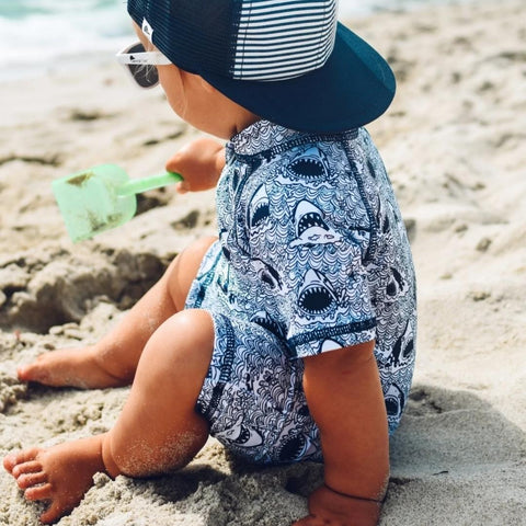 Young boy playing in the sand wearing a shark sunsuit