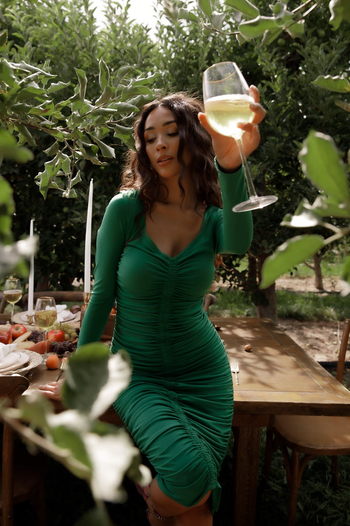 Model holding our RP wine glass, wearing RP Amazon Green Ruched Midi Dress