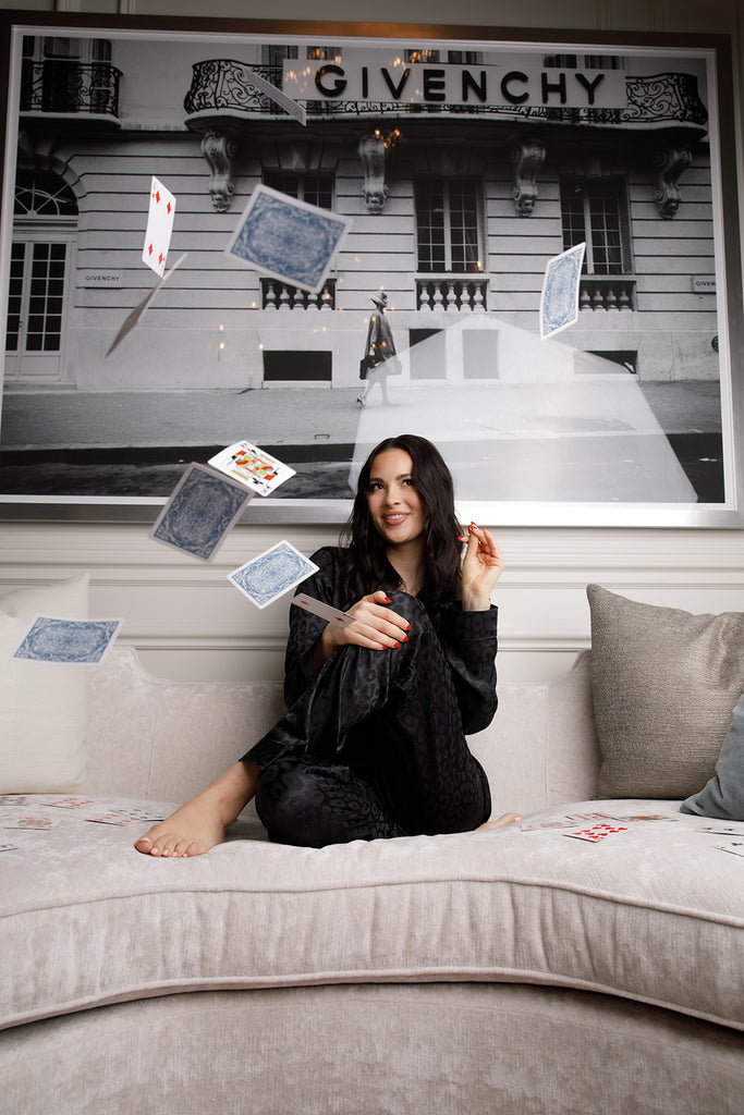 Rachel Parcell sitting on her couch, throwing playing cards, wearing the Black Satin Jacquard Cheetah Long Sleeve Pajama Set