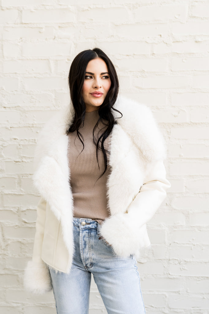 Rachel Parcell standing outside of her house in front of white brick wall wearing White Faux Fur Coat