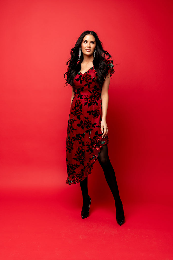Rachel Parcell in photo studio with red backdrop wearing Burnout Rose Deep Red Asymmetrical High Low Midi Dress