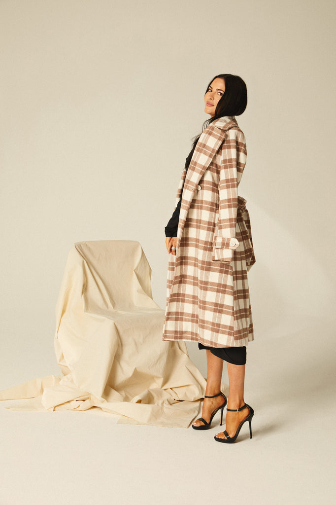 Rachel Parcell standing in photo studio looking over her shoulder at the camera wearing Black Asymmetric Jersey Dress with Plaid Tailored Overcoat draped over her shoulders