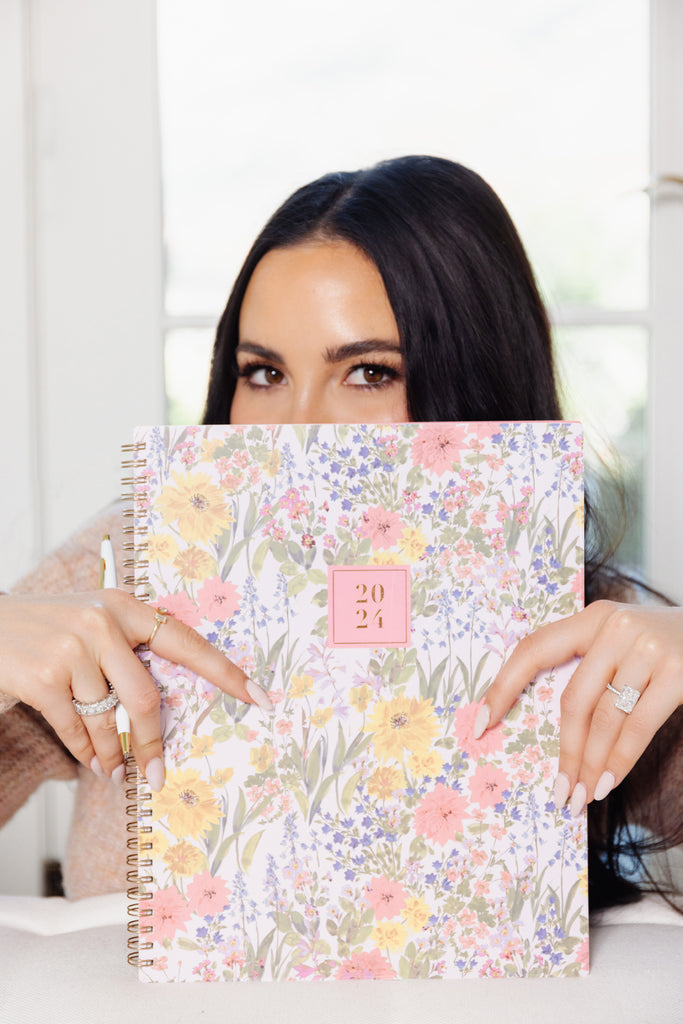 Rachel Parcell holding Blue Sky x Rachel Parcell planner in "Emily Pink" print in front of face with her eye's peeking over