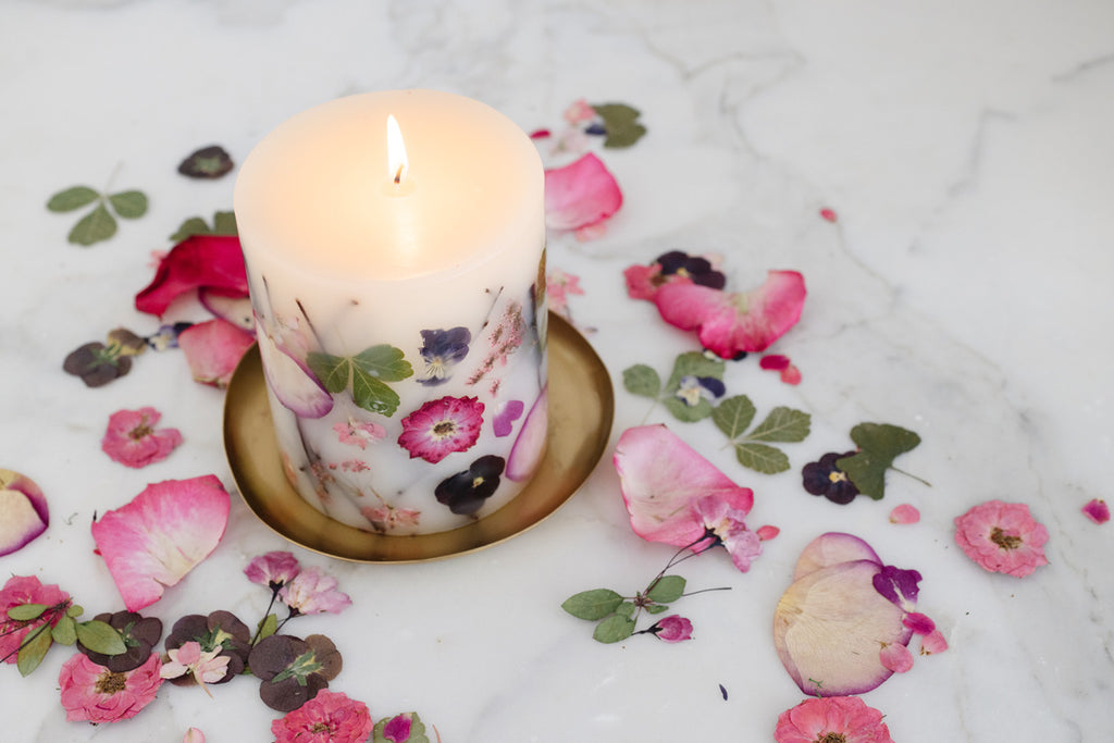 Lit Rosy Rings Peony Botanical candle surrounded by flower petals 