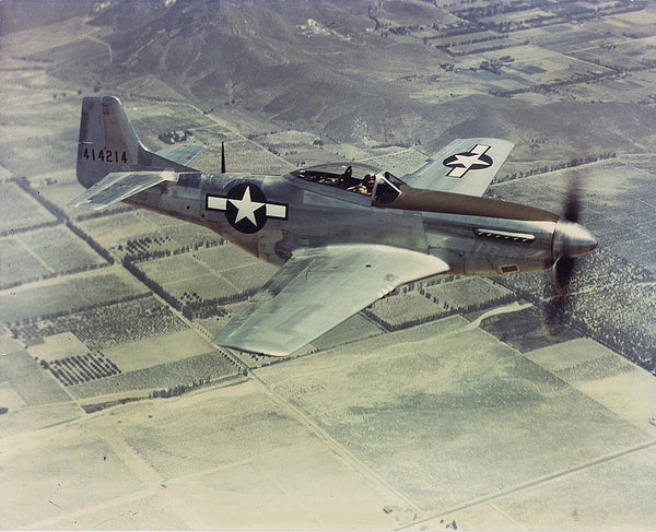 An historic North American P-51 Mustang in flight above American crop fields.