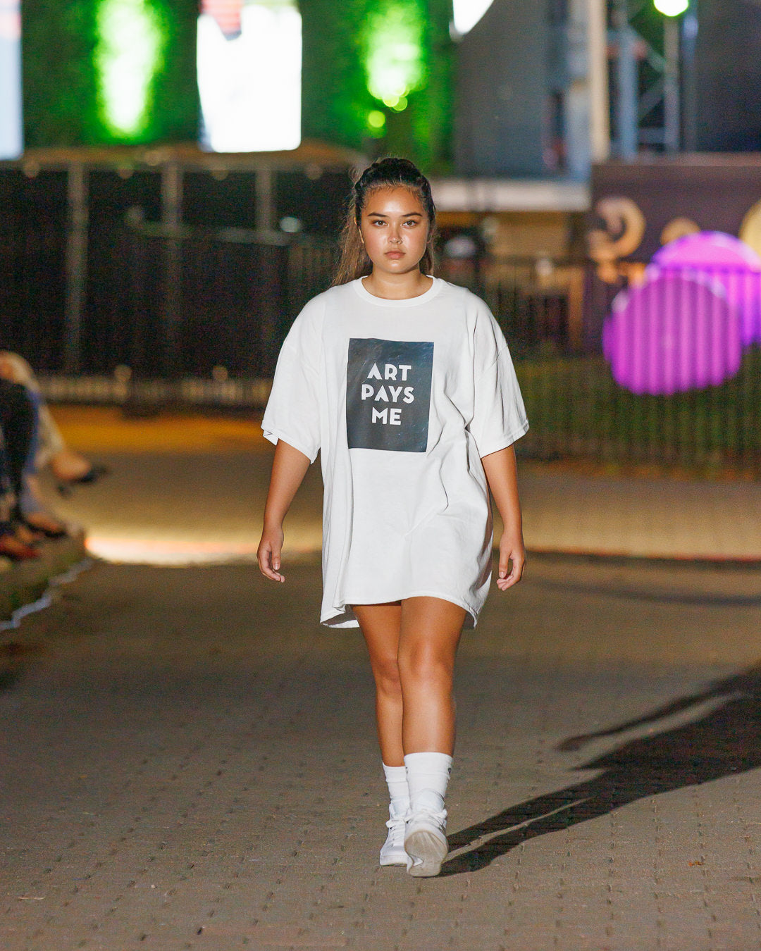 Girl wearing a white t-shirt with Art Pays Me printed on it