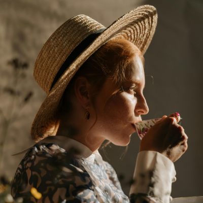 A woman with a hat sipping on a cup of chai tea.