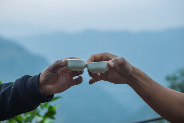 Two hands clinking two small cups of tea with the hills in the background