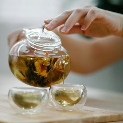 Tea being poured through a transparent teapot into a pair of transparent cup.