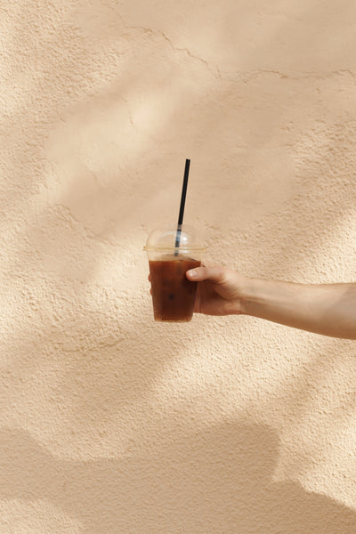 A takeaway cup with iced black coffee against peach wall background