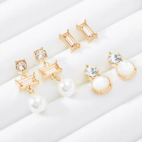 Three pairs of different drop and stud crystal earrings are set into a white jewelry display box.