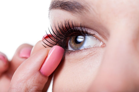 woman holding up fake eyelash to her eye