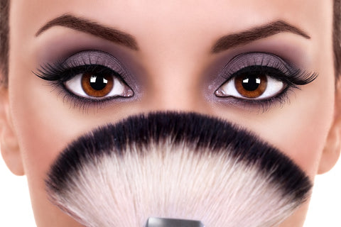 woman holding a makeup brush hiding her nose and mouth with made up eyes. 