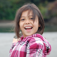 Christia Zeiter at age seven laughingly pretending to throw a rock at the photographer while on a camping trip with her family in the Redwoods of Northern California.