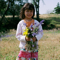 Alisandra Zeiter at age five with curly hair and a smile holding wildflowers from Our Lady's Ranch.