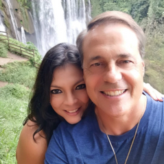 Philip Zeiter & Karen Marmol. Middle-aged couple in smiling in front of a waterfall in Honduras.