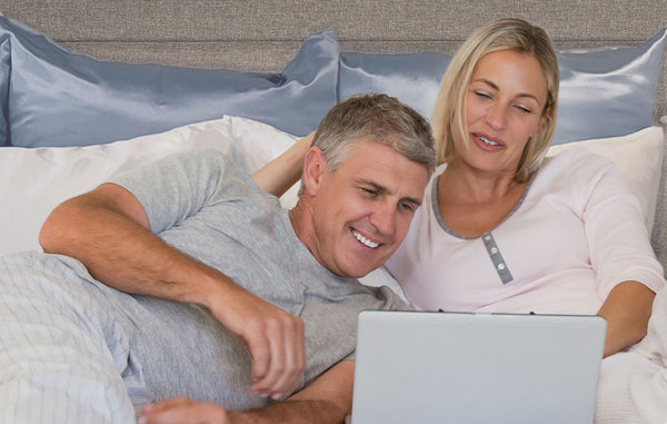 a couple laying in bed on silk pillowcases