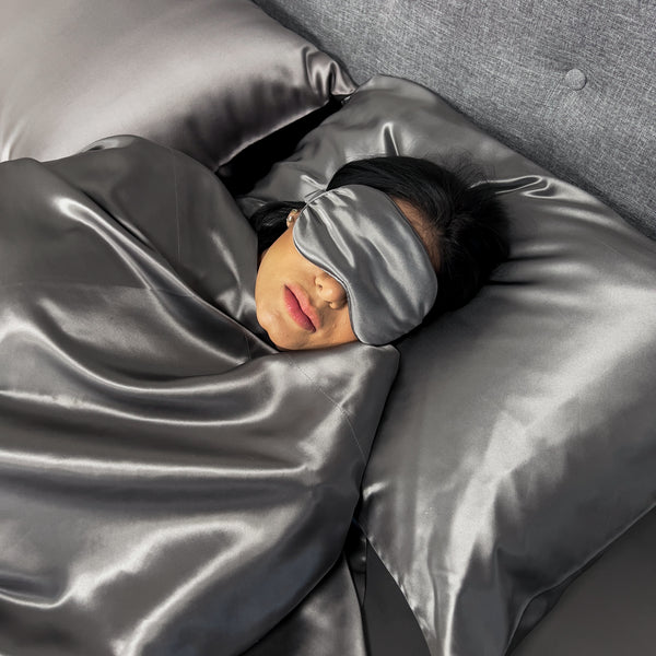 Model sleeps on silver silk pillowcase wearing matching sleep mask