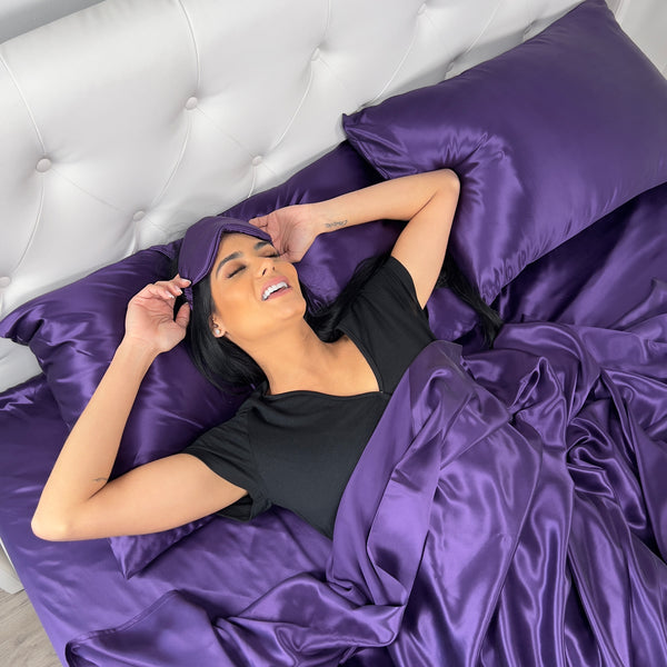Model in plum sheets smiling while wearing plum sleep mask