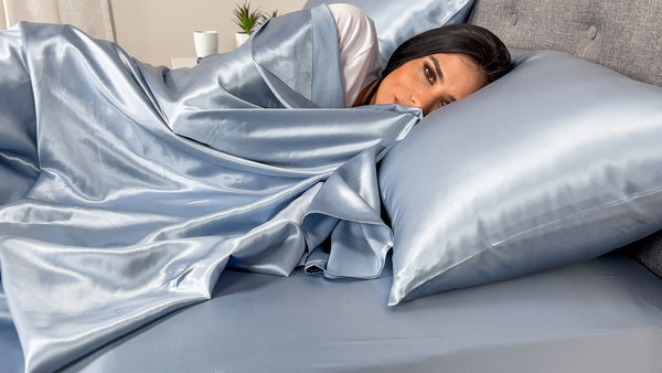 Model sleeps on steel blue silk pillowcase and matching sheet set