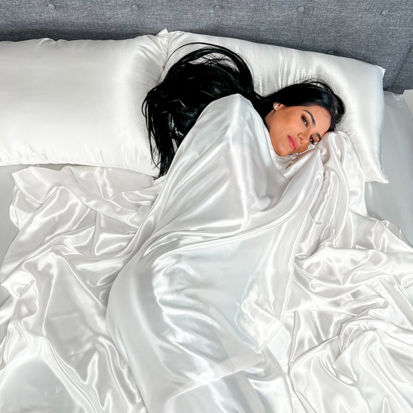 Dark haired model sleeps in white silk bedding, wrapped in a shiny silk top sheet