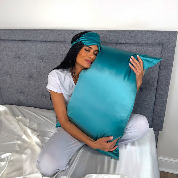 Model Holding Silk Pillowcase while wearing matching sleep mask in teal