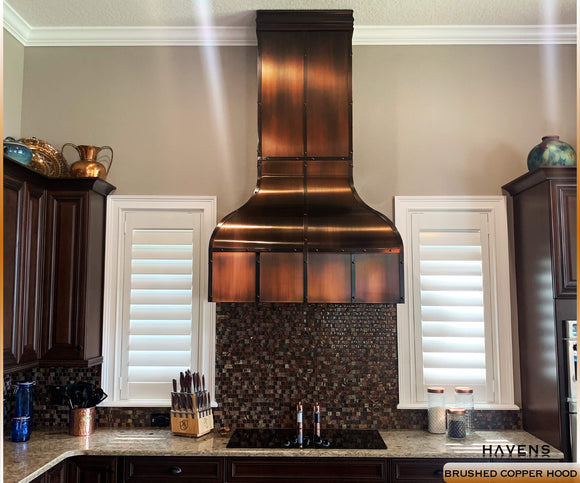 Copper range hood with a farmhouse kitchen sink, granite counters, and copper lighting