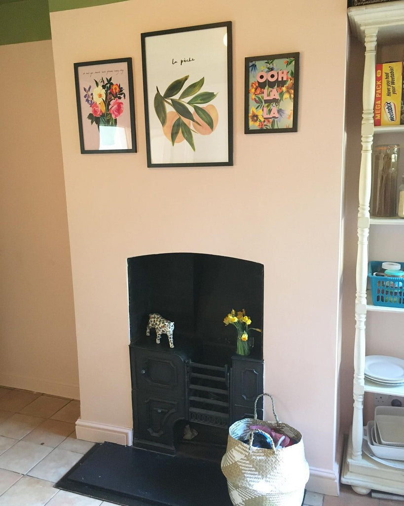 A pink painted dining room with original fireplace and a bright, peachy print hanging above 