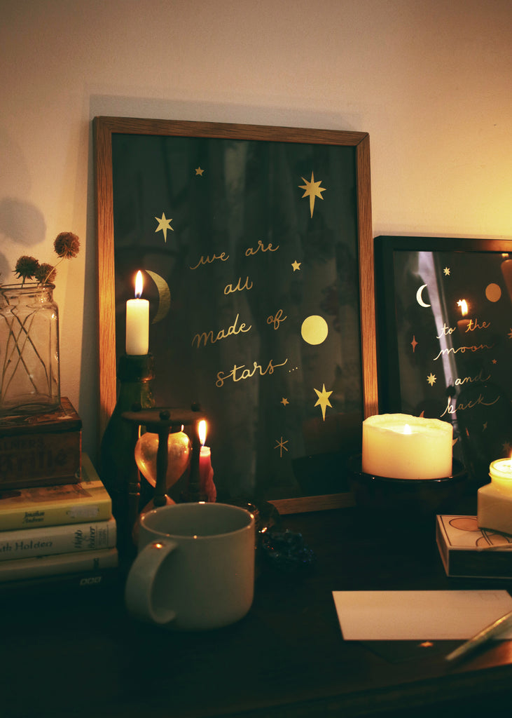 celestial print with gold foil in a wooden frame, surrounded by candles