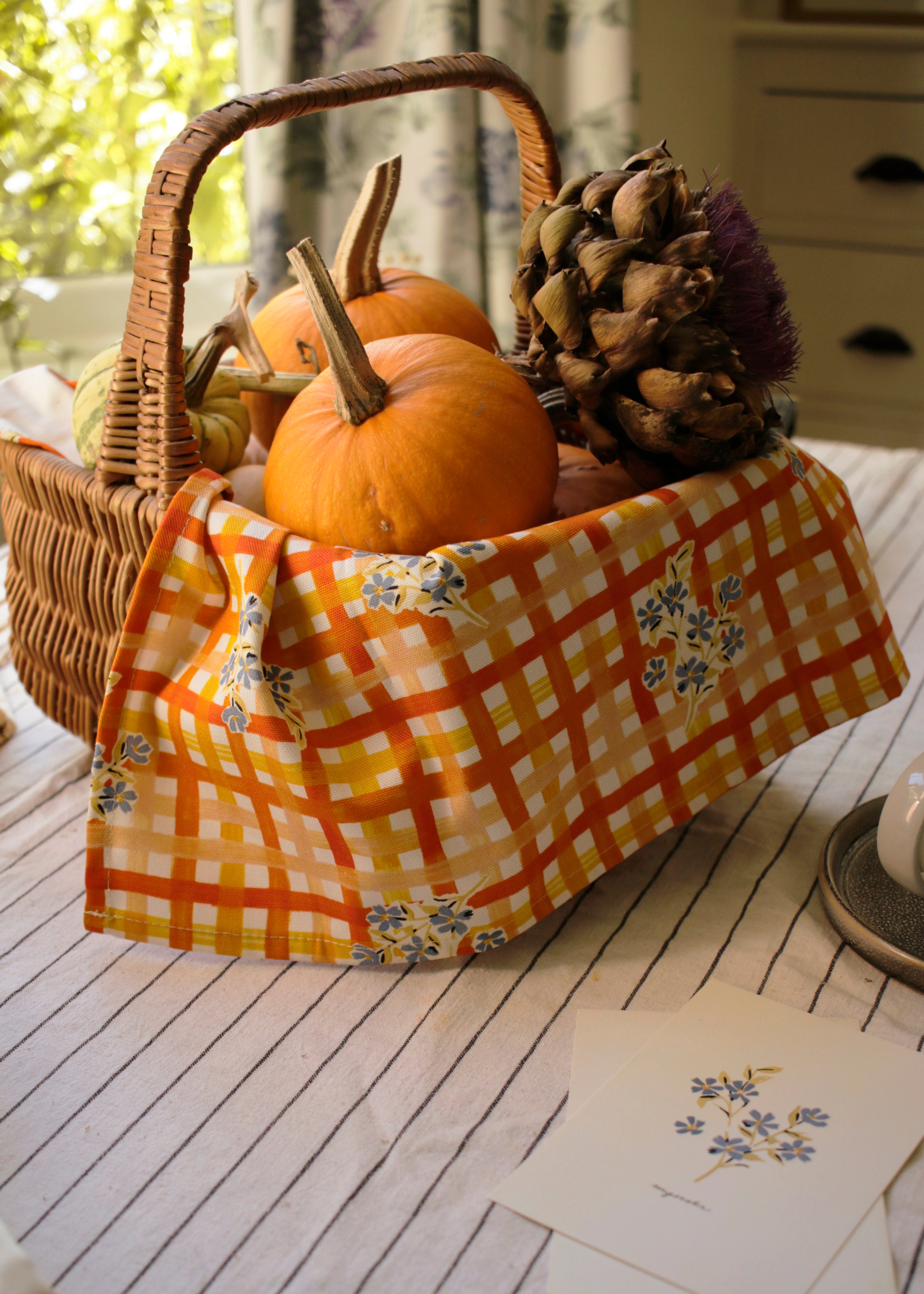 A floral and gingham patterned tea towel, tucked inside a wicker picnic basket