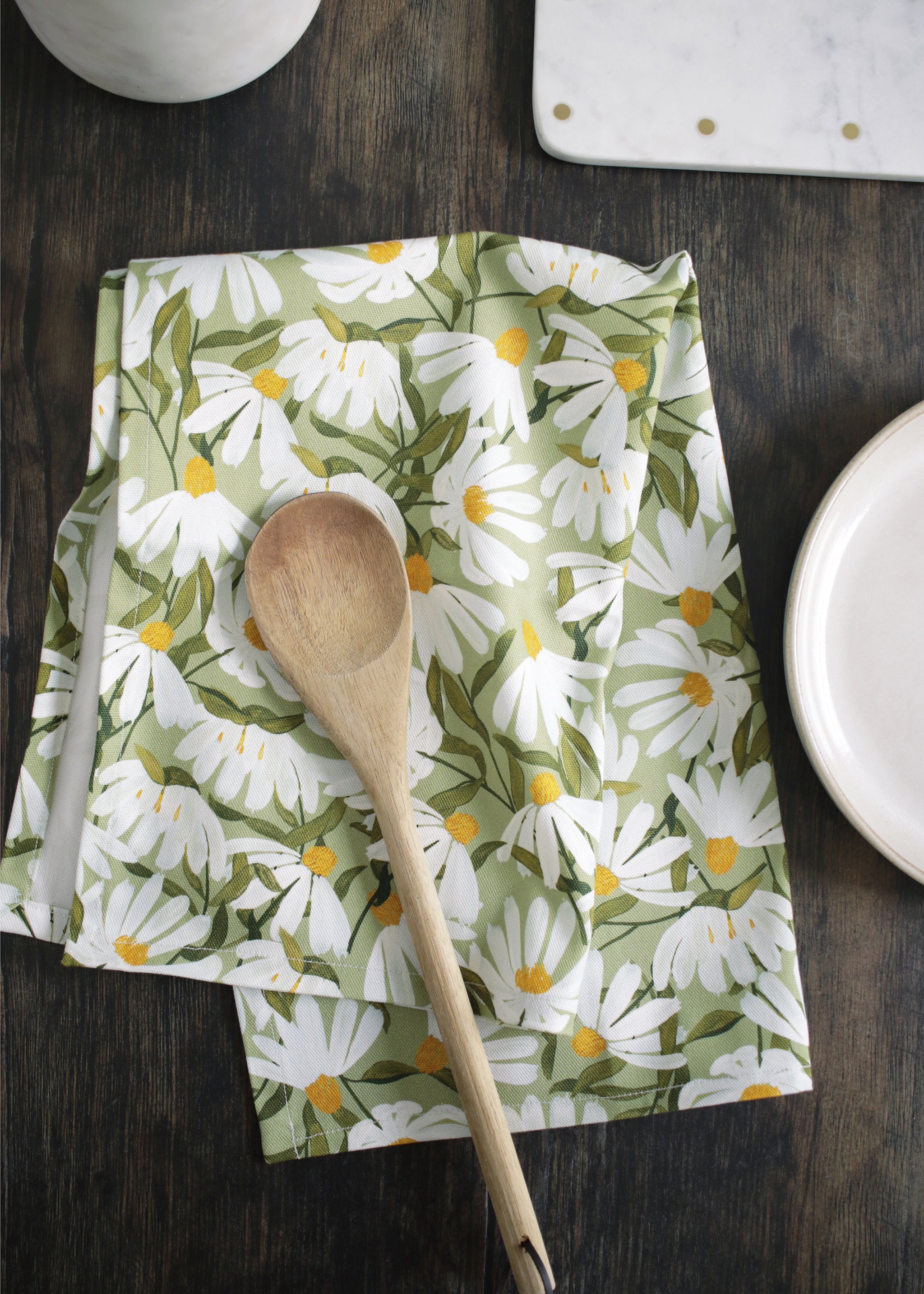 A green and white floral tea towl, folded ontop of a wooden kitchen table