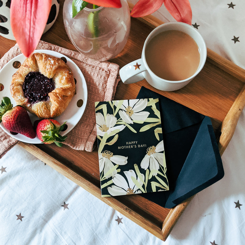 a floral mother's day card sitting on a breakfast in bed tray of coffee, pastries and flowers 