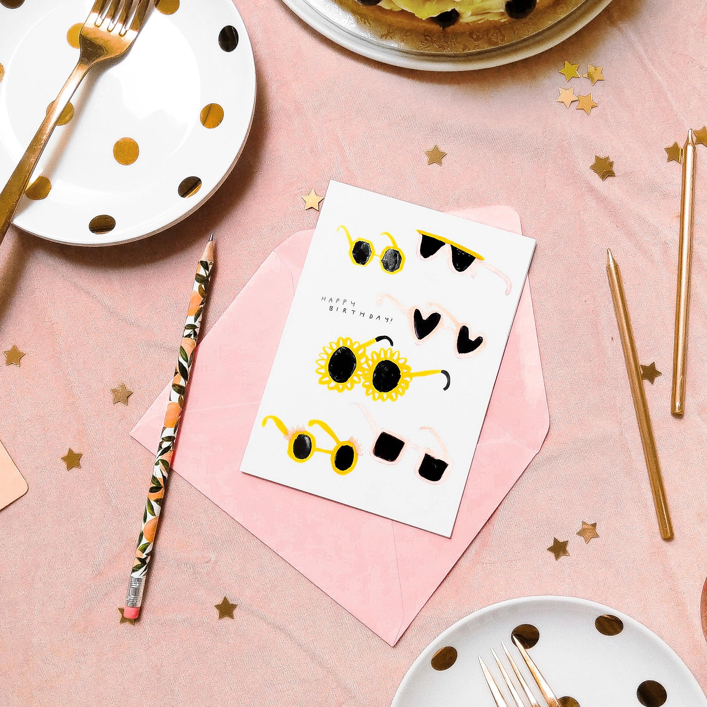 a white card with illustrated sunglasses on, on a pink party tablecloth