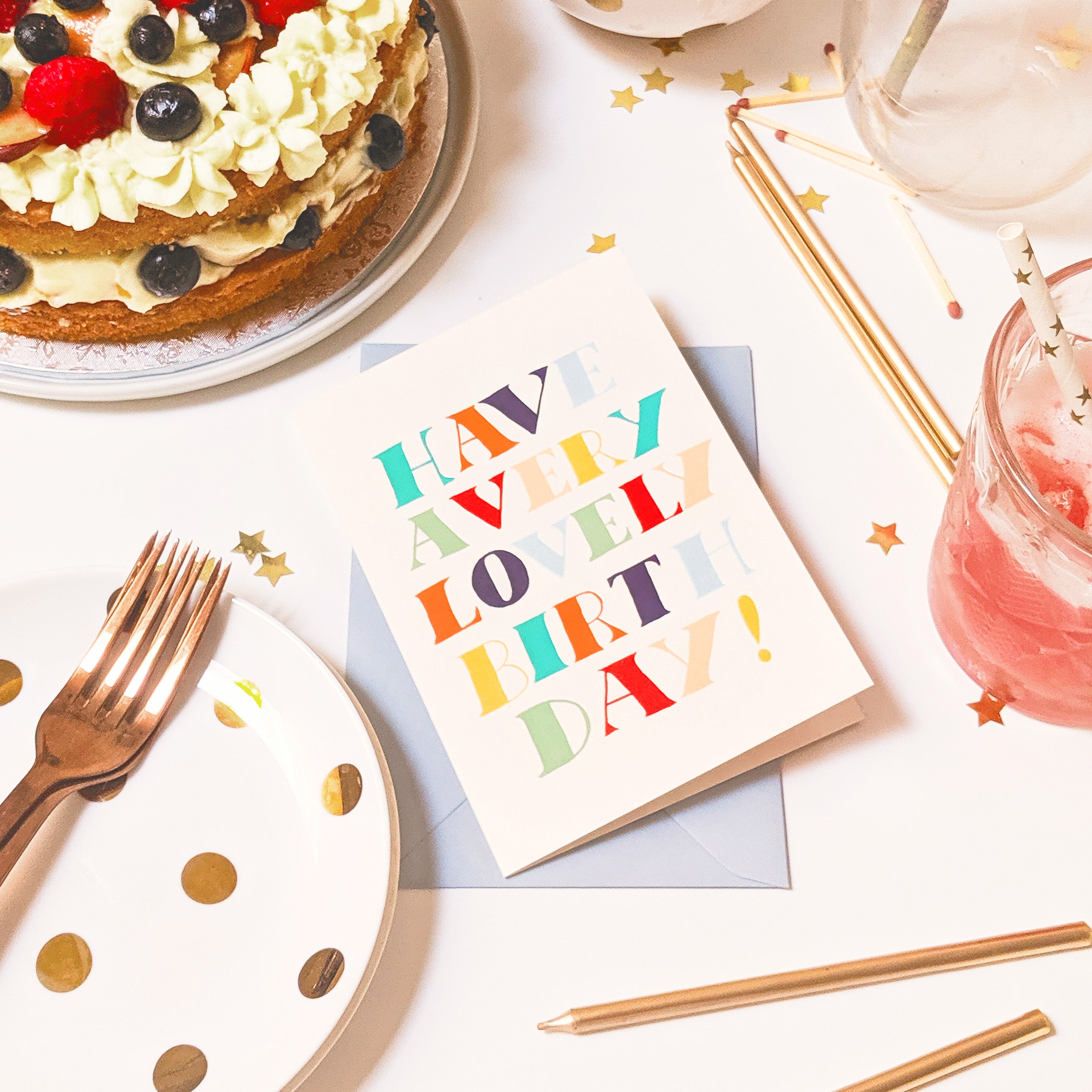 a typographic birthday card surrounded by cake, candles and drinks