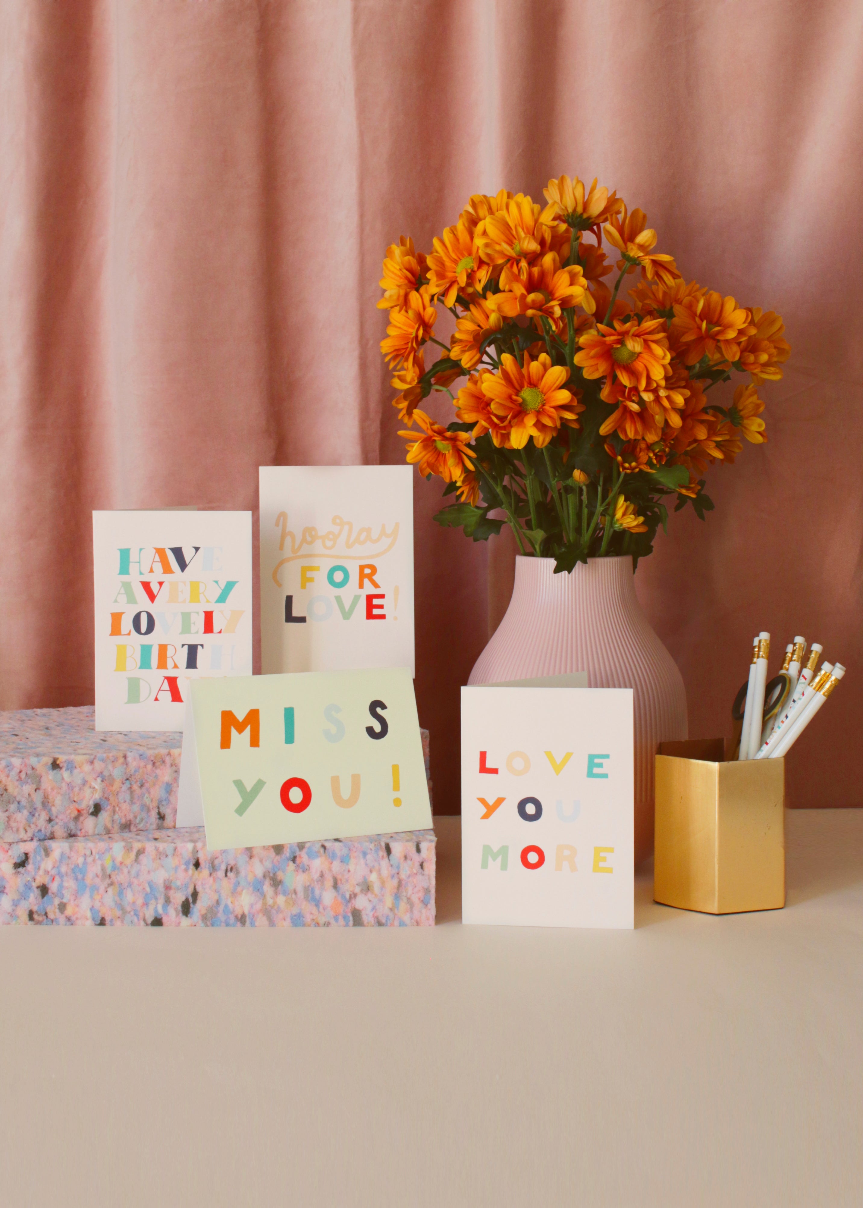 cards from the Super Love collection with orange daisies infront of a pink curtain