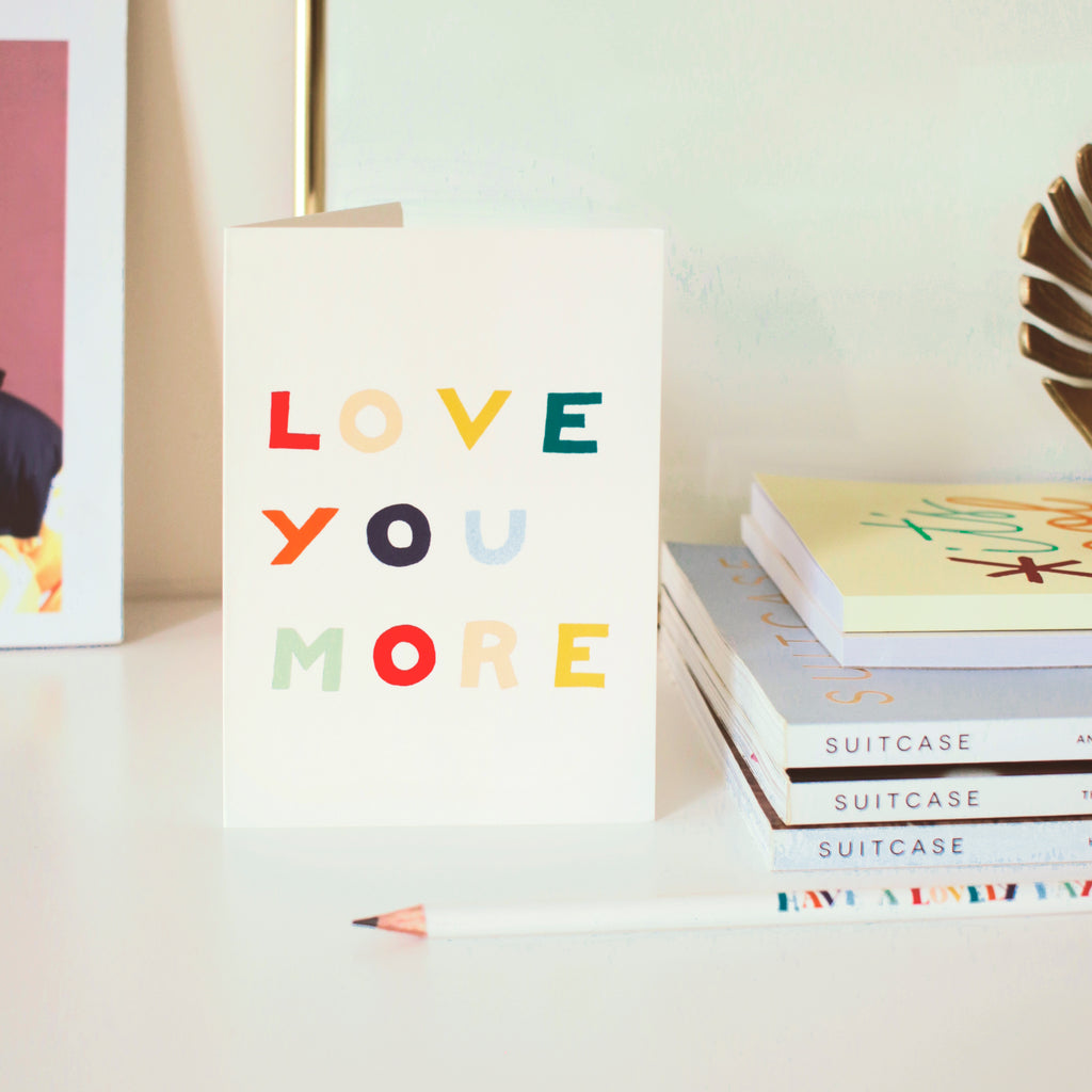 a rainbow-hued greetings card reads "Love you more" in block letters